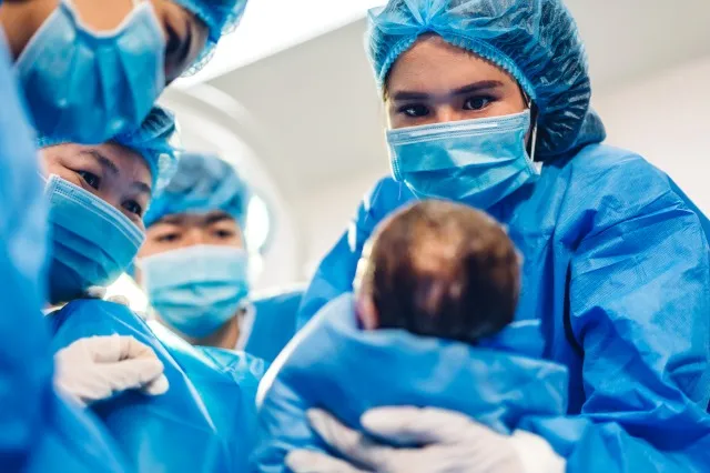 プロの麻酔医の医師の医療チームとアシスタントは、赤ちゃんの帝王切開を行っており、現代の病院の手術室で手術器具を使って赤ちゃんを出産しています