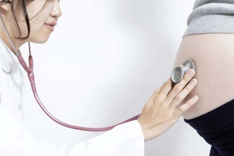 聴診器を妊婦の腹部にあてる医師
