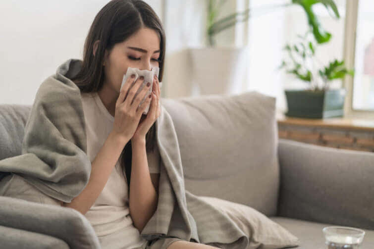 日常生活や健康問題のコンセプト：アジアの若い女性は風邪を引き、鼻を走らせたり熱を出したりして、自宅で休んで仕事を休まなければなりません。