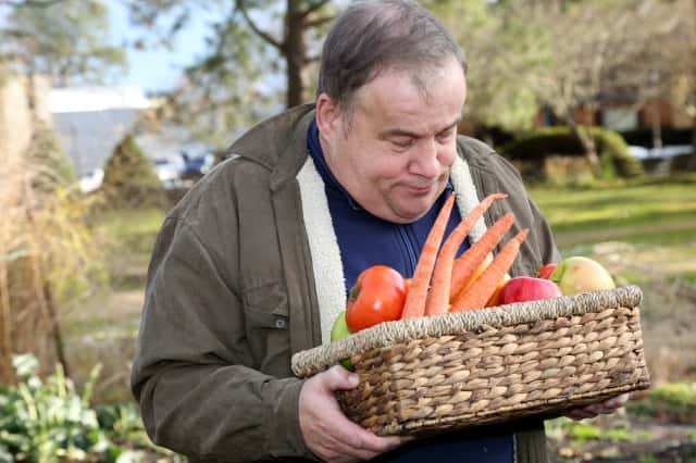 果物と野菜がいっぱい入ったバスケットを持つ庭で働く自閉症の男性
