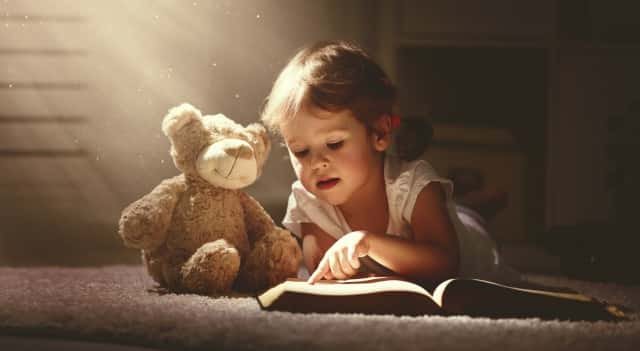 テディベアで遊びながら本を読む少女