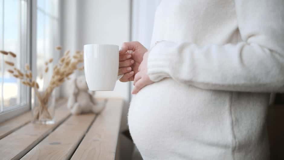 腹痛が収まってホッとしながら温かい飲み物を飲む妊娠中期の女性