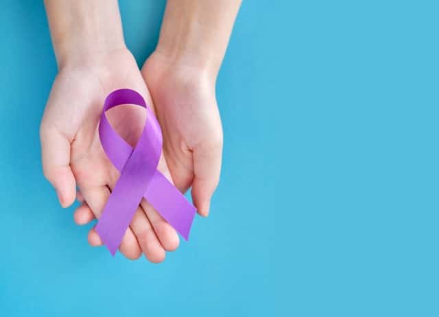 紫紫の象徴的なリボン - 膵臓癌、嚢胞性線維症、線維筋痛症の問題。 青色の背景に 2 つの交差させた手