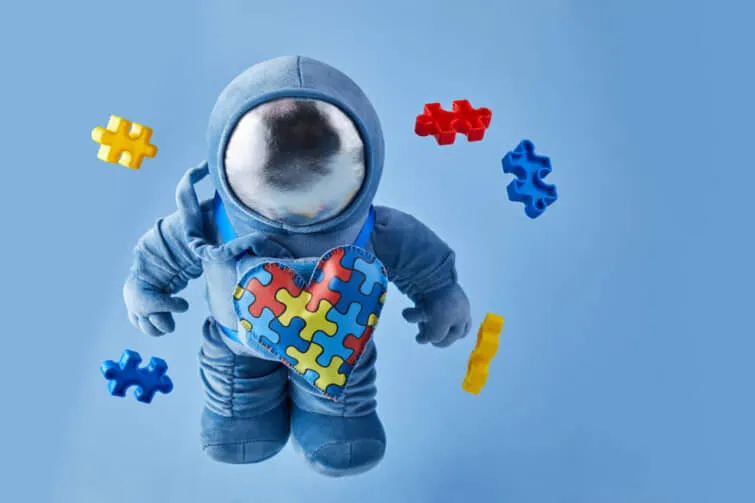 世界の自閉症認知の日の背景。 青の背景にパズルの心と自閉症のシンボルを持つ青いプラシ宇宙飛行士のおもちゃ