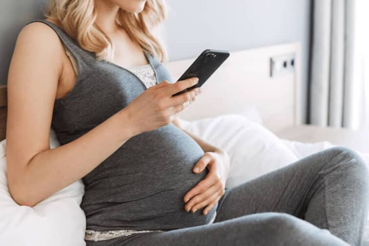 スマホ片手にお腹を撫でる妊婦さん