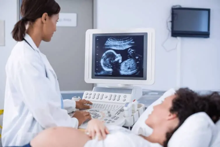 妊娠中の女性の腹部と腹部超音波検査の画面を見る医師