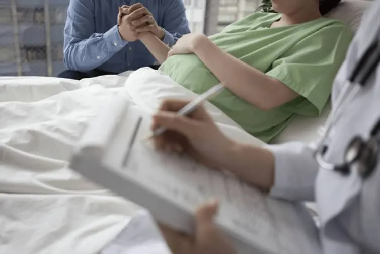 妊婦さんとベッドサイドで励ます夫とメモを取る医療職