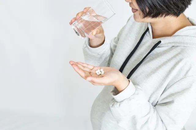 手に錠剤を持ちグラスで水を飲む大きなお腹の妊婦。妊娠、病気、服薬、病気イメージ