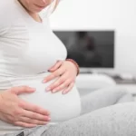妊娠中の疲れた疲れた女性は、自宅のソファで胃の問題を抱え、病気になっています。