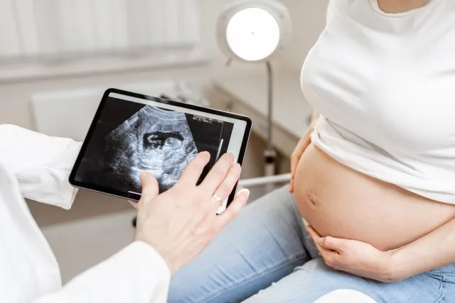 オフィスで妊娠中の女性との検査中にデジタルタブレットで胎児の超音波スキャンを行う医師、顔のないトリミングされたビュー