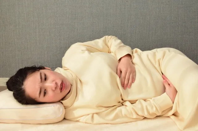 20代の妊婦さんが、つわりと苦しそうな顔で横になっています。