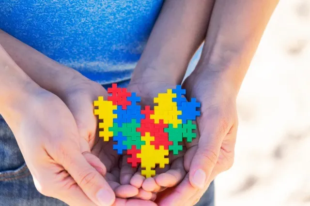 色とりどりのパズルの心を持った母親に支えられた自閉症の子供の手。 世界自閉症啓発デーのコンセプト