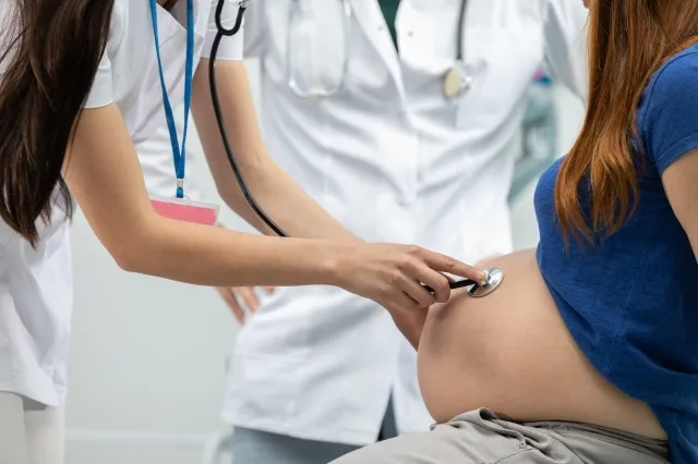 妊婦の腹部を聴診器で聴診する女性医師の拡大図。 専門医院