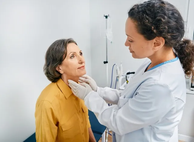医師は、診療所で甲状腺疾患や甲状腺機能低下症を診断するために、太った成熟した女性の首を触診します。 甲状腺治療