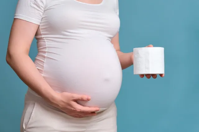 妊娠中の女性の手の中のトイレット ペーパー、青色の背景で撮影スタジオ