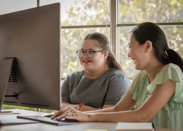 アジアの幸せな素敵な若いぽっちゃりダウン症候群の自閉症の自閉症の小さな娘と母親のポートレート ショットは、コンピューターを介してオンラインで学習しながらカメラを見て笑っています。 生徒にレッスンを教える先生