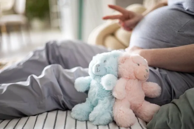 双子の男の子と女の子を待っている 2 本の指を身振りで示すクマのおもちゃで妊娠中の女性のおなかをクローズ アップ