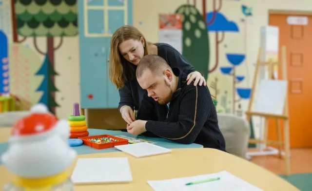 女性の心理学者が、オフィスで自閉症の成人した男の子と一緒に働いています。