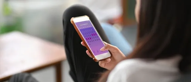 女性の手の中のスマートフォン画面で月経周期を監視するためのモバイル アプリケーション。 女性は携帯電話を持ってソファに座っています。
