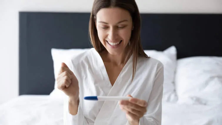 ベッドに座って妊娠検査薬で妊娠しているかチェックしている女性