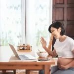 家庭で妊娠中に、話し合いや手を振る動画をオンラインで呼び出し、笑顔を見せるアジアの若い母親