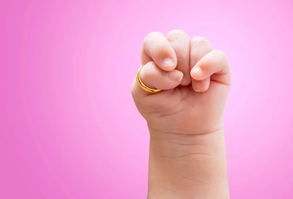 トリソミー18症候群の拳を握り締め、親指に金の輪を持つ幼児の手の接写