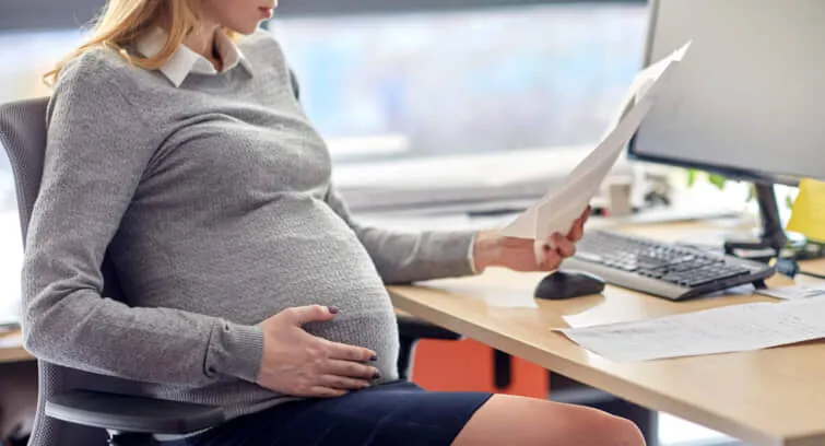 妊娠、ビジネス、および仕事のコンセプト – オフィスのテーブルに座り、書類を読みながら妊娠したビジネスマンにほほ笑みかける