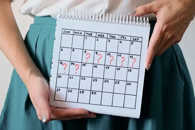 マークされた逃した期間のカレンダーを保持している女性。 望まない妊娠、女性の健康、月経の遅れ。