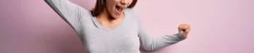 ピンクの背景に妊娠した若い美しい10代の女性が、幸せで明るく、微笑み、気軽に自信を持って音楽を聴く