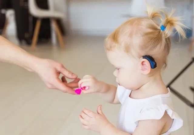 女の赤ちゃんの耳に補聴器。 家で補聴器を装着している幼児。 障害児、障害、難聴のコンセプト。