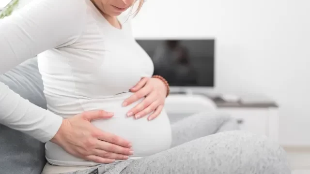 妊娠中の疲れた疲れた女性は、自宅のソファで胃の問題を抱え、病気になっています。